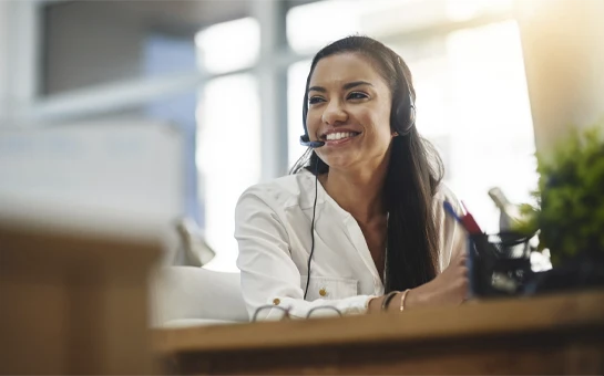 Person wearing a headset seated at a desk with office supplies visible in a workplace setting.
